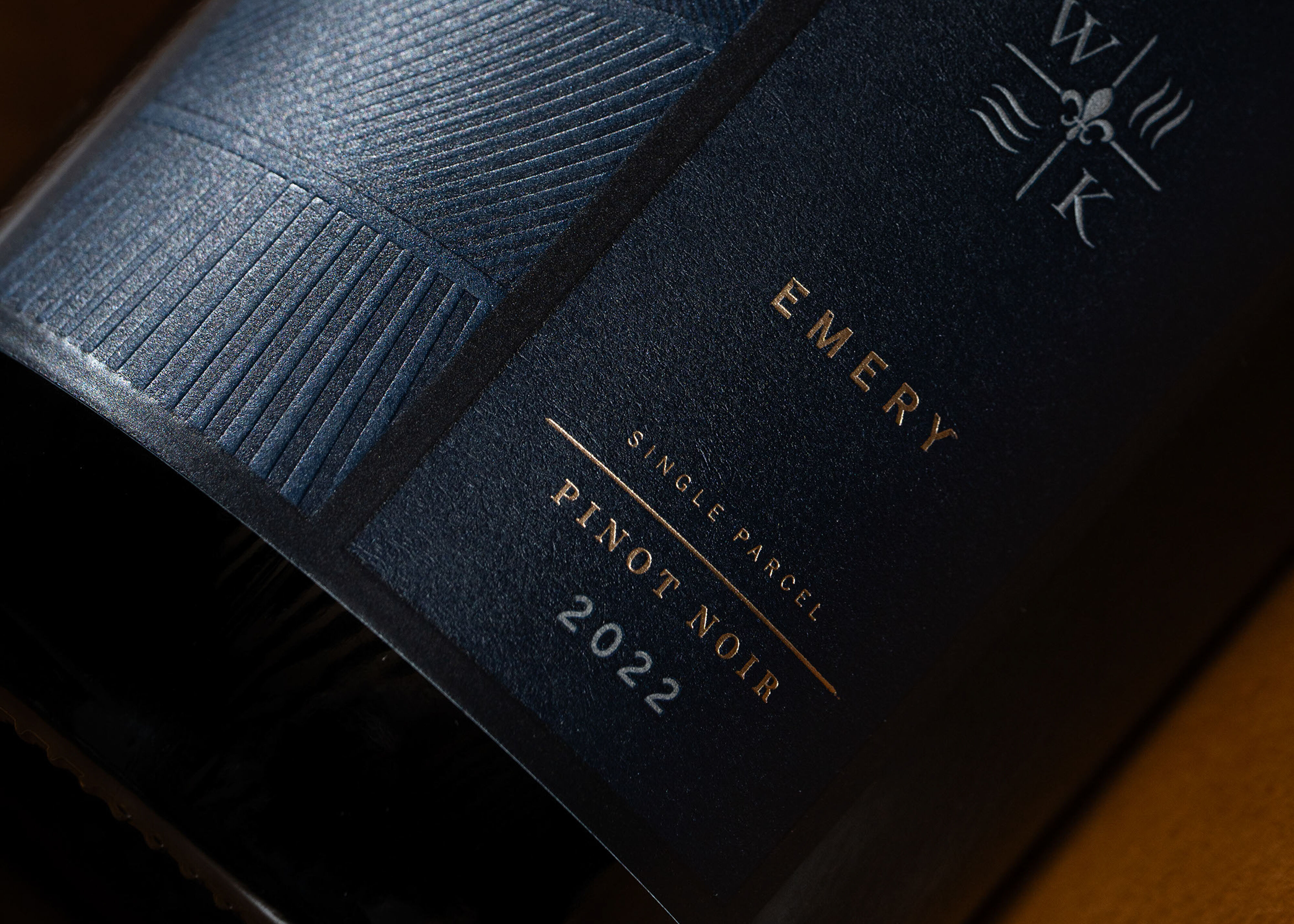 Three bottles of wine laying on wooden furniture next to books, a lamp and a glass of red wine.