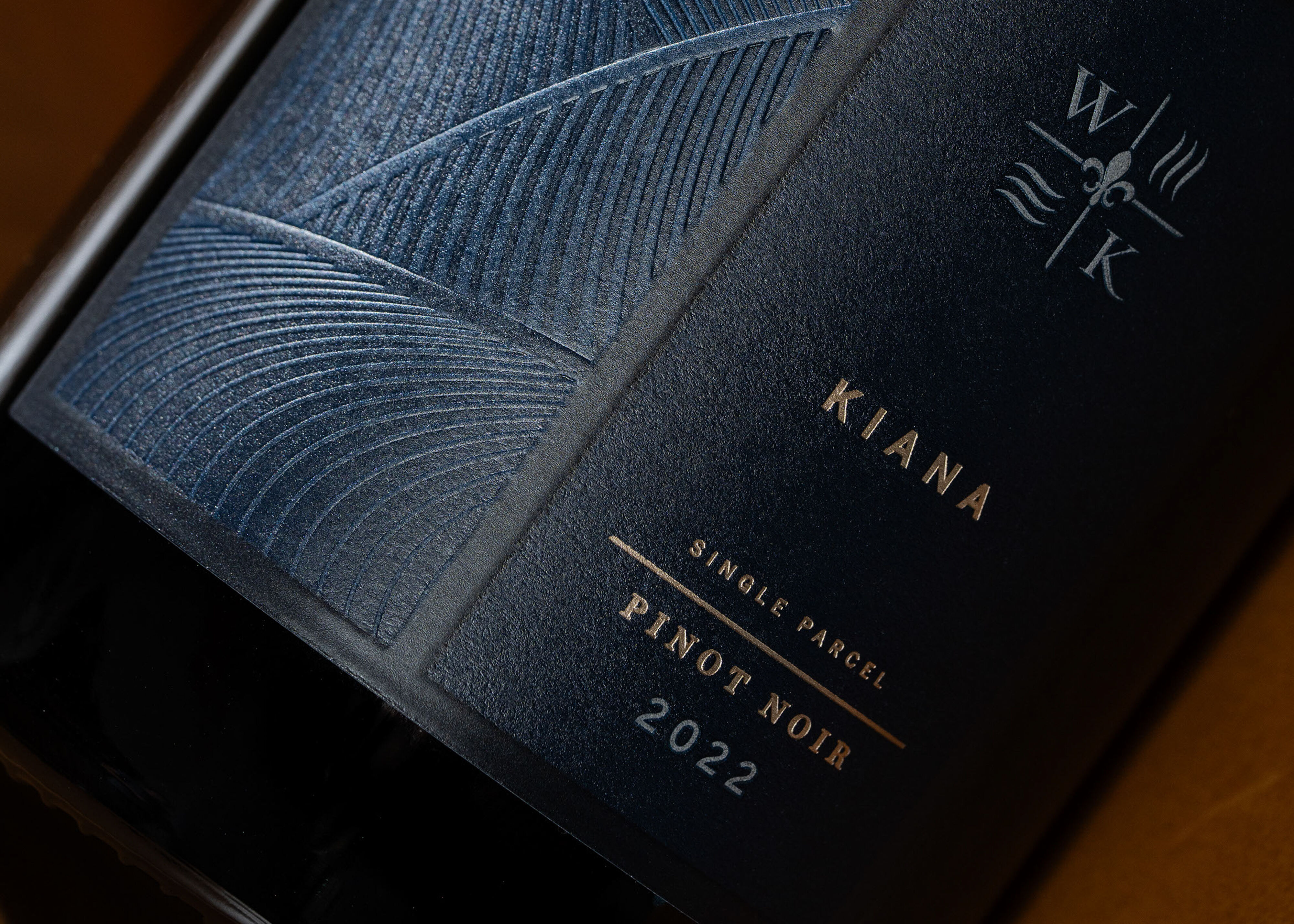 Six bottles of wine laying on wooden furniture next to books, a lamp and two glasses of red wine.